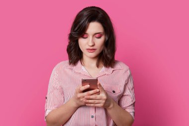 Kahverengi saçlı kız öğrenci düşünüyor, ne onun değmek perde telefon ile oldu ve kafa güzel boyalı gözler ile asılı. Genç benzersiz kadın Merkezi izole açık pembe renkli üzerinde duruyor.