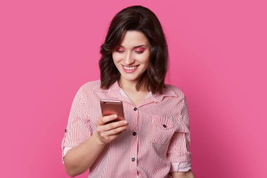 ?öldüme, sevgili kadın kişi smartphone izole pembe portre fotoğrafçılığı ortasına gülümseme görünüyor. Onun Kahverengi kıvırcık parlak makyaj konumlandırıldığı yüzünde harika görünüyorsun.