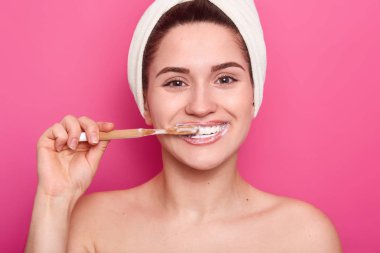 Diş Bakımı kavramı. Memnun genç kadın parlak bir beyaz gülümseme parlayan dişleri vardır, ahşap diş fırçası ve pembe arka plan üzerinde izole beyazlatma diş macunu ile diş temizler, doğal güzelliğe sahip.