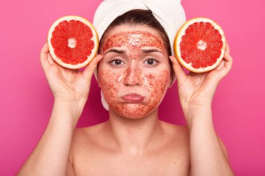 Üzgün memnun genç kadın izole shot fırçalayın fasial maskesi, greyfurt iki dilim tutar, beyaz havlu üzerinde kafası, sağlıklı ve güzel olmak istiyor, hizmet spa salonda sevmez.