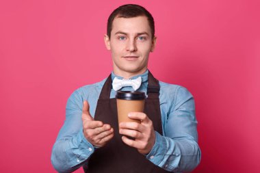 Dost erkek barista tat aromatik kahve onun tarafından yapılan için öneriyor, sıcak içecek palm tek kullanımlık bardak ile gösterir, şık gömlek ve pembe arka plan üzerinde izole önlük giyer. İçki kavramı