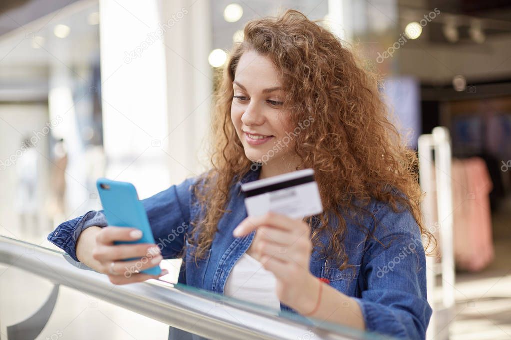 Stylish and bright woman reads notice that lot of money was received on account. Agitated mistress checks information on internet. She holds credit card in hand, checks availability of funds.