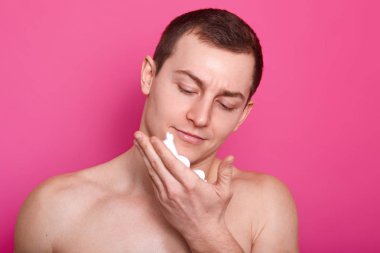 Tıraş kremi onun Palm'da şaşkın adam fotoğrafı. Yakışıklı çocuk elinde görünüyor, çıplak omuz, pembe bir arka plan üzerinde izole vardır. Kısa saç modeli adamla. Cilt bakım ve erkeklik kavramı.
