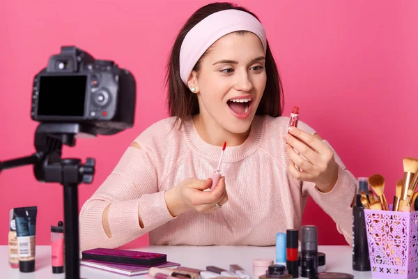 Belleza blogger con cámara dispara nuevo video para su vlog. Morena mujer anuncia productos cosméticos. Mujer joven sostiene lápiz labial y brillo. Chica hace vídeo lección de cómo ponerse maquillaje . — Foto de Stock