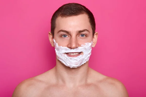 Närbild porträtt av stilig man med raklödder på hans ansikte som isolerade över rosa bakgrund. Man rakar skägget i badrummet. Ung pojke ogillar borst. Vardagliga förfarande. Hudvård och koncept. — Stockfoto