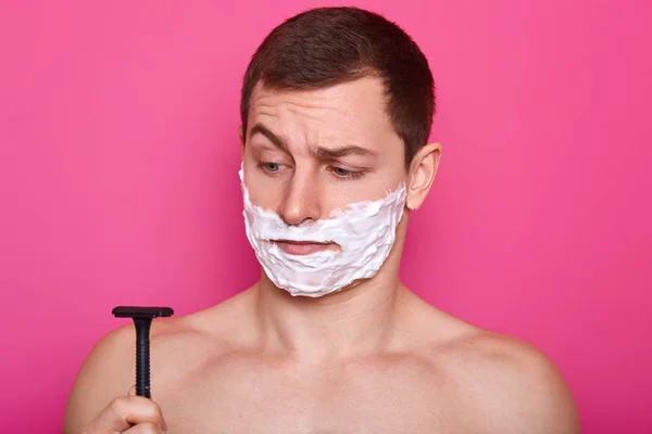 Headshot przystojny mężczyzna wygląda inn zakłopotanie w razor, ma golenie żel na policzkach, ma codziennej rutyny w łazience, na białym tle różowy, chce mieć gładką skórę. Koncepcja utrzymania higieny — Zdjęcie stockowe