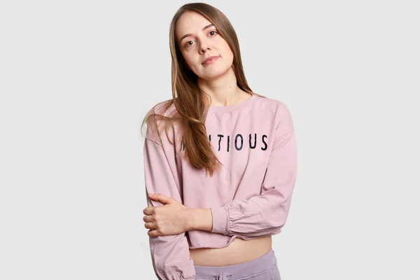 Tiro de media longitud de la mujer europea contemplativa serius mantiene las manos parcialmente cruzadas oves pecho, vestido con sudadera suelta casual, tiene cuerpo delgado, aislado sobre fondo blanco, posa en el estudio —  Fotos de Stock