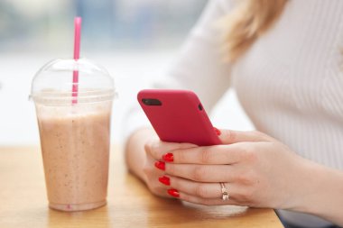 Meçhul kadın modern cep telefonu elinde tutan, kırmızı manikür vardır, bildirim, saman ile plastik fincan içecekler milkshake kafeteryasında kablosuz internet bağlı denetler. Teknoloji kavramı
