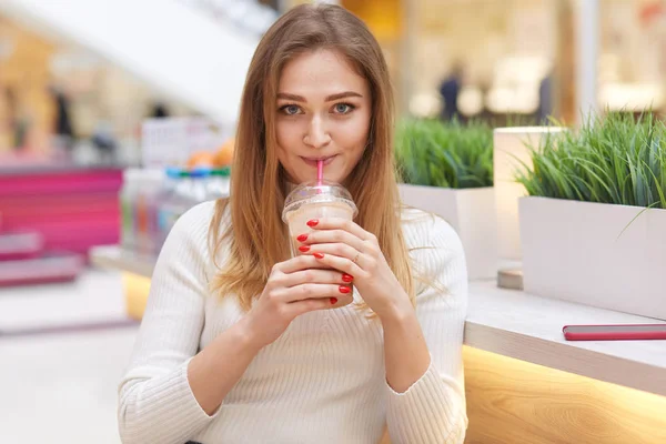 Image d'une jolie jolie femme vêtue de pull blanc, tient un cocktail au lait, regarde la caméra, passe du temps libre avec des amis, visite différents magasins et cafés, a manucure rouge. Temps de repos — Photo