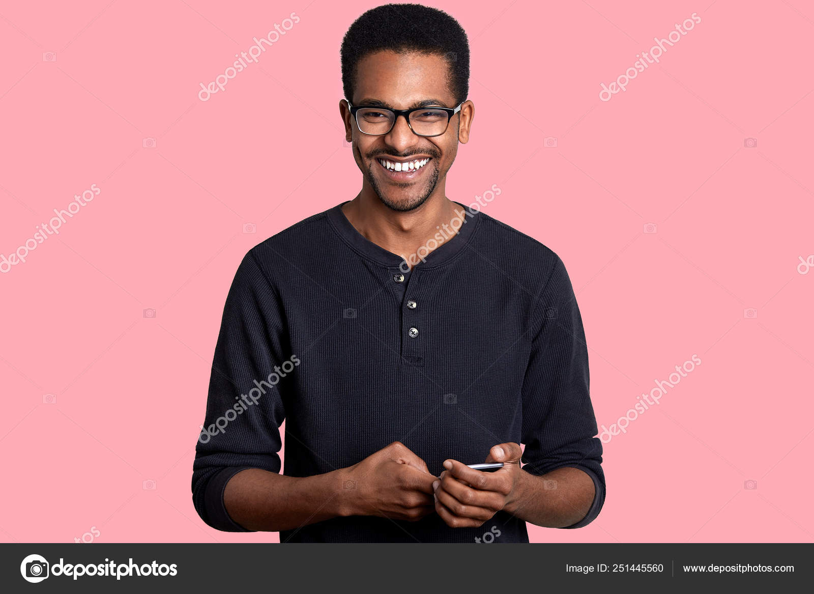 Handsome Young African American Man Holds Smart Phone And Looks At Camera With Smile Has Great News From Friend Dark Skinned Model Poses Against Pink Background People And Technology Concept Stock Photo