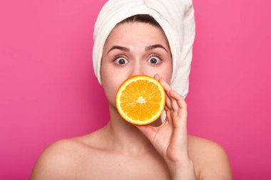 Havlu kafa ve Malaysian omuzlarında ile güzel sürpriz kız portresi. Geniş açık gözlü çekici kadın ağzını yarım portakal ile kapsar. Erkek Cilt Bakımı yordamının spa salonda vardır..