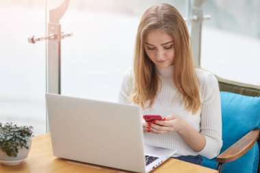 Genç kadın onu laptop ile çalışmamaya kafede masada oturur ve akıllı telefonunu alır. Kız kablosuz internet kullanır. Kadın telefonu tutan ve onun ekran isoleted kafe penceresinde görünüyor.