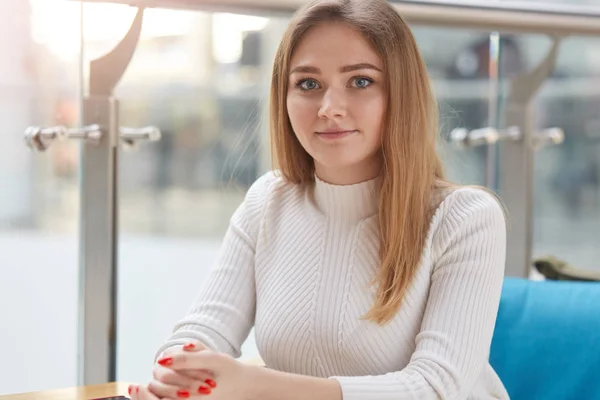 Ritratto di bella ragazza con pelle perfetta. Donna bionda guarda la macchina fotografica con le dita incrociate, trascorre il suo tempo libero in un caffè, si riposa dopo l'università, attende il suo ordine. Concetto di gioventù e studenti . — Foto Stock