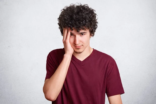 Portret van de jonge jongen met weinig baard en krullend donker haar, houdt hand op tempel geïsoleerd op een witte muur, sufers van hoofdpijn, onthoudt gisteren partij. Studenten, jeugd en levensstijl concept. — Stockfoto