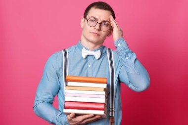 Görüntü fo genç öğrenci adam holding yığını kitap ve having baş ağrısı, tutar el başında, modeli pozlar gül studio arka plan üzerinde doğrudan kameraya benziyor. Alan metni kopyalayın. Eğitim kavramı.