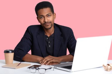 Dizüstü bilgisayar, kamera, görünüyor axuasted ile çalışan yakışıklı Afro-Amerikan erkek alarak fren fotoğrafı yüz ifadeleri üzerinde pembe arka plan izole bozdu. İnsanlar kavramı.