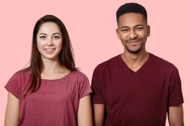 Portrait of beautiful young couple looking smiling at camera, on pink wall background, wears casual t shirts, have cheerful facial expressions, being in good news, have great news. People concept. clipart