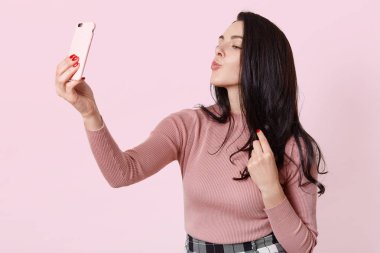 Çekici kız selfie için smartphone kullanarak fotoğraf. Uzun siyah saçlı çekici Bayan selfie yapar, yuvarlak, dudakları yüz ifadesi öpüşme ile poz kadın koruyamaz. İnsanlar ve fotoğraf kavramı.