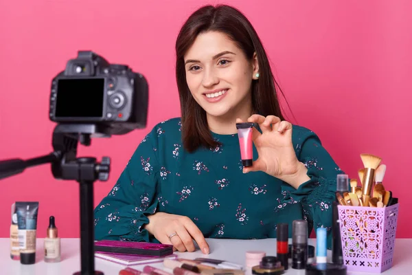 Famoso blogger. Mujer alegre mostrando productos cosméticos durante la grabación de vídeo y dar consejos para su blog de belleza, mira a la cámara digital, tiene expresiones faciales agradables. Concepto publicitario . — Foto de Stock