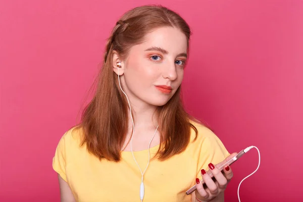 Headshot dari remaja carming, memiliki smartphon dan earphone, menikmati mendengarkan musik selama waktu luang, mengenakan pakaian santai, terisolasi di atas latar belakang merah muda. Remaja, pemuda dan konsep hiburan . — Stok Foto