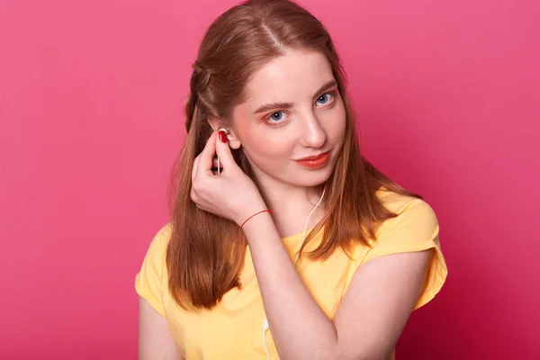 Muchacha joven y atractiva pone auriculares, listo para escuchar música, se ve irónicamente en la cámara, lleva una camiseta de color amarillo brillante, tiene el pelo liso marrón, pasar tiempo libre a solas. Concepto de personas y entairtaiment . —  Fotos de Stock