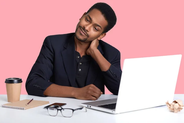 Knappe Afro-Amerikaanse man zit aan Bureau, dragen van klassieke jas, op zoek zeer moe, zijn handen op zijn nek, voelt pijn, kijkt opzij en probeert om te ontspannen, on line werkt gebruikt wi fe. — Stockfoto