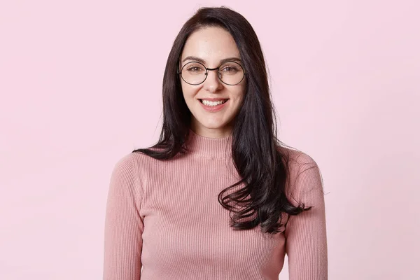 Κοντινό πλάνο του σκούρα μαλλιά Ευρωπαϊκό θηλυκό με στρογγυλά γυαλιά, φοράει πουκάμισο, απομονωμένη πάνω από ροζ τοίχο. Γοητευτική γυναίκα έχει ευρύ χαμόγελο, να είναι σε καλή διάθεση, μετά την ημερομηνία με το φίλο. — Φωτογραφία Αρχείου