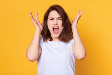 Doğrudan kameraya, bir şey, çığlık izole sarı arka plan üzerinde duran sevimli genç bayan arıyorum görüntüsünü eller baş yakınındaki tutar, beyaz casual t gömlek giyer. Kopya alanı reklam için.