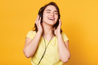 Sarı arka planda müzik dinlemek güzel bir kadın. Kapalı eyess ile poz Bayan dinleme favori müzik hoşlanır, charming eller kulaklıktan tutar, şarkı söylüyor ve rahatlatır. Yaşam tarzı kavramı.