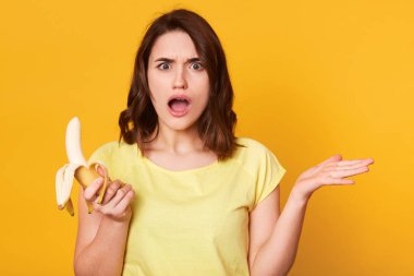 Taze muz, tutan güzel genç kadın yan için ele alır, sarı arka plan açık ağız ile ayakta erdirilemez yüz minderlerle vardır. Reklam veya promosyon için kopya alan.