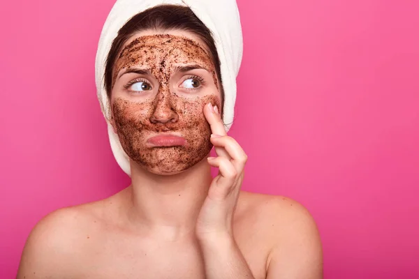 Menina bonita com toalha branca na cabeça. Feminino encantador aplica o scrab cosmético. Tratamentos de beleza em casa. Cuidados diários com a pele. Mulher fica com lábios malcheirosos contra a parede do estúdio. Conceito de cuidados da pele . — Fotografia de Stock