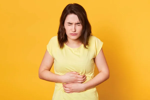 黄色の背景にひどい腹痛と若い白人女性のポートレートを食べる何か有効期限が切れて、中毒には、目を閉じて立っているし、腹 hamd を保持を閉じます。健康の概念. — ストック写真