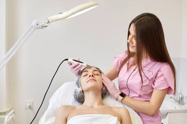 Vrouw ontvangt ultrasone gezicht afschilfering op cosmetologie salon. Procedure clearing verstopte poriën, ultrasone behandeling voor huidverjonging, schoonheidsspecialiste maakt gebruik van moderne apparatuur voor het vernieuwen van — Stockfoto