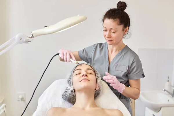 Jonge aantrekkelijke vrouw krijgen van ultrasone gezichtshuid zuivering behandeling door professionele schoonheidsspecialist, in de schoonheidssalon. Dermatologie maakt verfrissende procedure. Huidverzorging en verjonging concept. — Stockfoto