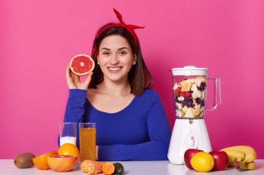 Onun elinde kesilmiş meyve tutan gülümseyen pozitif kadın portresi. Genç model, Smoothie 'nin hazır olmasını bekler. Neşeli mutlu kadın zevk ile sağlıklı diyet sopa. Sağlıklı yaşam konsepti.