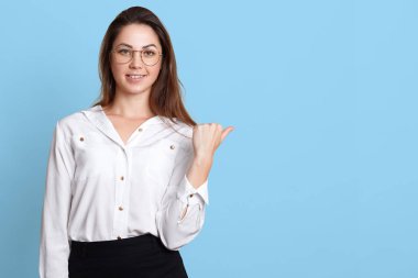 İyi görünümlü genç işçi beyaz bluz, siyah etek ve şık gözlük giyer, mutlu çalışma günü sonuna geliyor görünüyor, yönü gösterir. Gülümseyen enerjik kız iş onun yerine memnun.