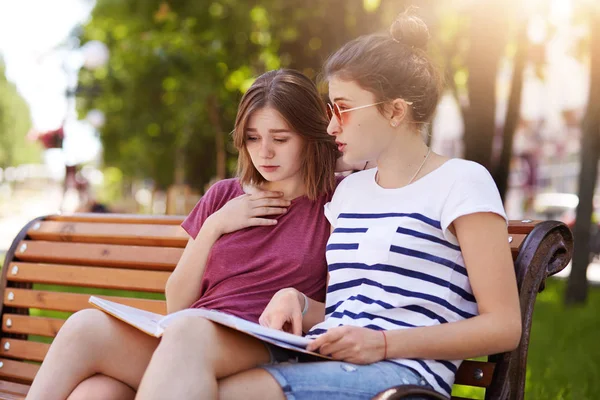 Cheerful funloving girls look through final issue of local magazine, discuss new events and people. Curious friends show their interest in public life, express their opinions. Friendship concept. — Stock Photo, Image