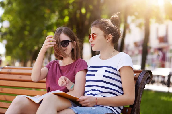 Chicas alegres felices están en el parque para disfrutar de la atmósfera de verano y leer las últimas noticias del mundo. Jóvenes amigos hermosos dan comentarios divertidos a cada foto y se ríen en voz alta. Concepto de amistad . — Foto de Stock