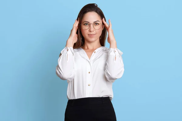 Fatiguée travailleuse de bureau intelligente masse ses tempes à cause de maux de tête, porte une blouse blanche et une jupe classique noire, des lunettes à la mode, se tient fermement sur son sol, rêve d'avoir un bon repos . — Photo