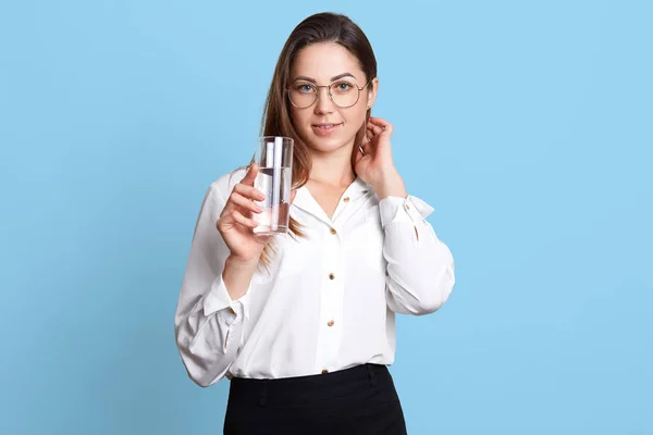 Hermosa mujer trabajadora puso hebra de su cabello detrás de la oreja, sostiene un vaso de agua en su mano. Atractiva linda dama se siente sedienta, pero feliz de tener la oportunidad de beber. Concepto de vida oficina . — Foto de Stock