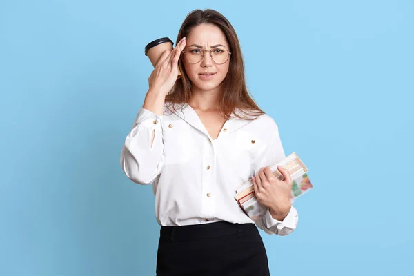 Jovencita cansada toma su mano con café cerca del templo, tiene un montón de libros en la mano, se siente mal, dolor de cabeza horrible. Mujer linda ocupada tiene demasiadas tareas tediosas que hacer. Estudio y concepto de trabajo . — Foto de Stock