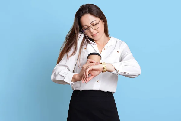 Busy well skilled young employee looks at her watch, holds paper cup of coffee, talks on phone, staying positive with tight schedule. Business and office working concept. Copy space for advertisement. — Stock Photo, Image