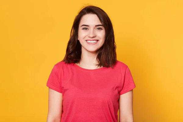 Retrato de joven hermosa chica tiene la piel perfecta y sonrisa tooyht, se pone de pie sonriendo, mirando directamente a la cámara, tiene expresión facial feliz, se ve satisfecho, posando aislado sobre el fondo amarillo . —  Fotos de Stock