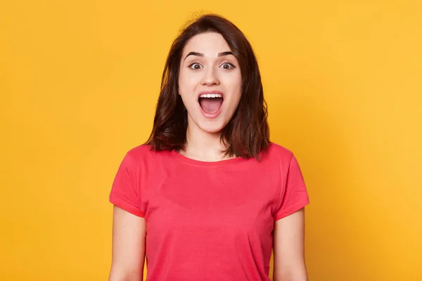 Mujer joven sorprendida gritando sobre fondo amarillo, mirando a la cámara, se ve feliz, tiene noticias maravillosas, estar de buen humor, contento de escuchar algo agradable, posando en el estudio. Gente concepto de emoción — Foto de Stock