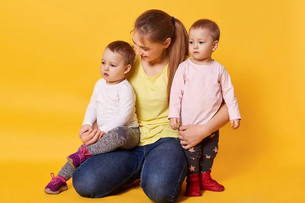 A smiling woman sits with her fair-haired daughters, hugs kids a — Stock Photo, Image