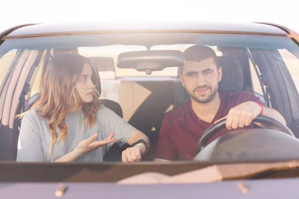 Couple travelers reach destination by car, beautiful woman tells somethig her husband at wheel while sitting at front seat. Young family has long trip or journey, enjoing spending time together.