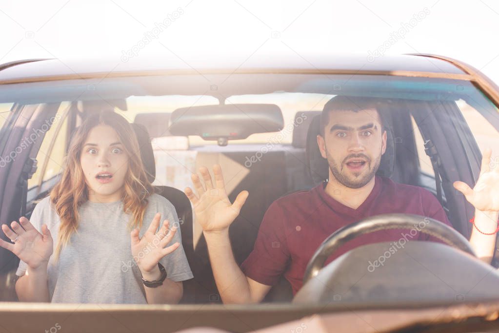 Shocked couple in car, indicate at windscreen with terrified expression as see awful accident on road, female drives car, young family sit with opend mouths in auto, have journey or trip. Road concept