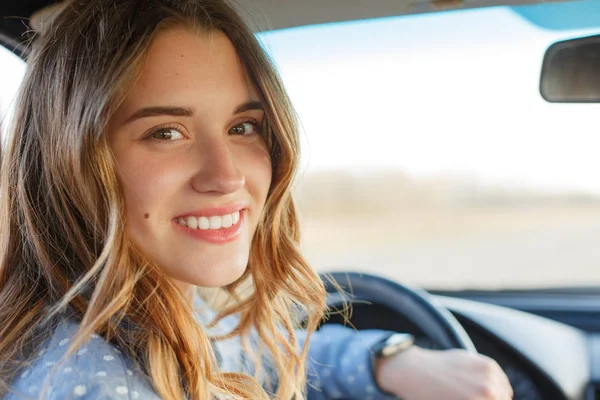 Back View van aantrekkelijke vrouw in de auto, zittend op het wiel, draaien en kijken naar de passagiers in de achterbank. Mooie vrouwelijke kijkt naar camera met toothy glimlach, die blij zijn om examen in driving school Pass. — Stockfoto