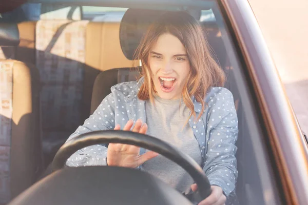 Retrato de bela jovem no carro novo, dirigindo seu automóvel primeira vez, apita para o marido feliz, tem um presente maravilhoso para o seu aniversário. Mulher atraente gosta de comprar veículo . — Fotografia de Stock