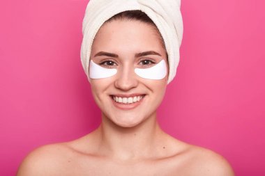 Close up portrait of half naked woman with rowel on head, has perfect skin, has no make up, with patches under eyes isolated on pink studio wall background. Health care and cosmetic procedures concept clipart